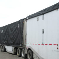 Two white chip truck trailers with a black trailer roll tarp on each one with one closed and one open.