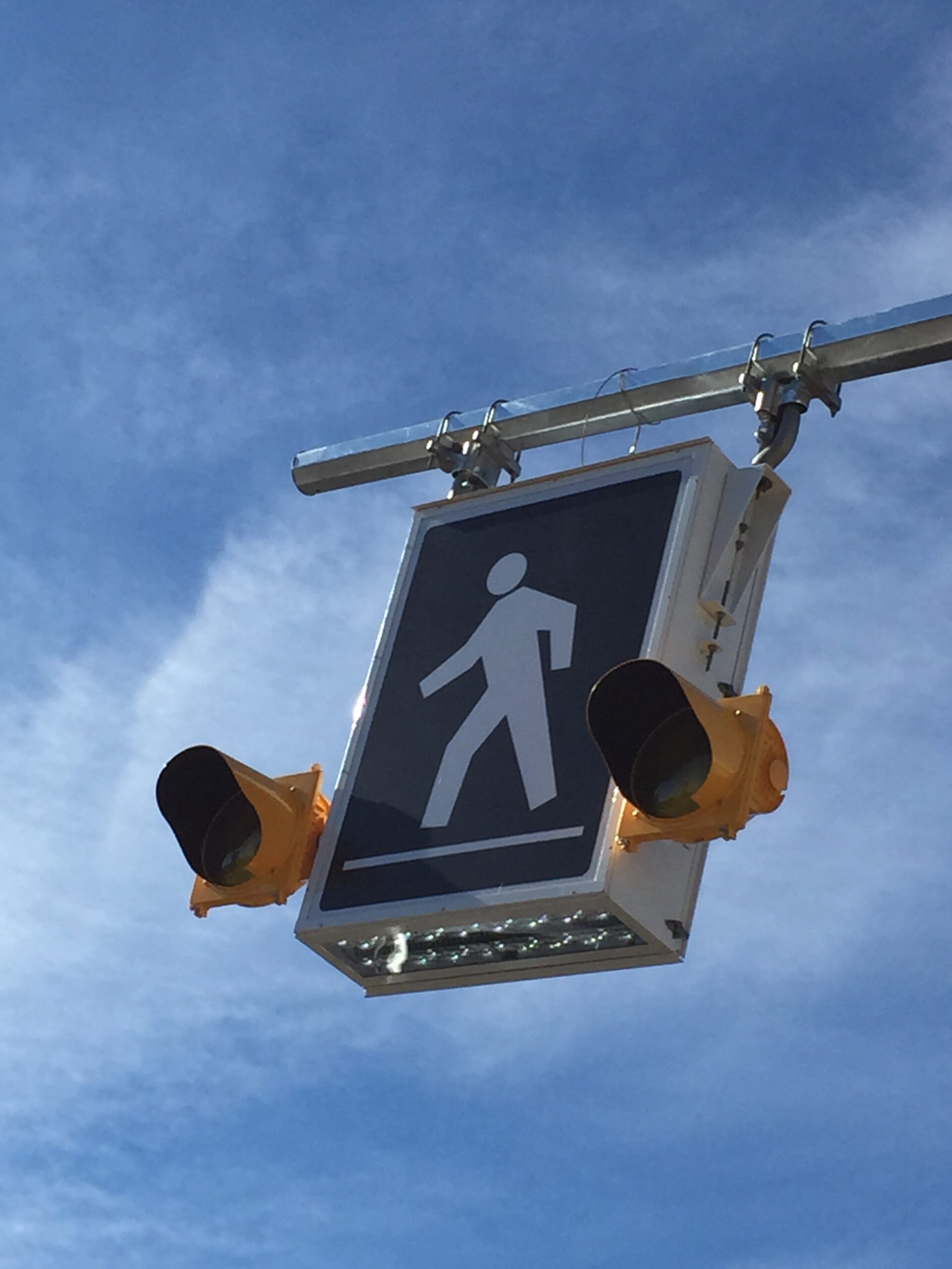 Looking up at an LED pedestrian crosswalk sign with a blue sky behind it.